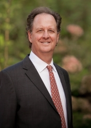 white man with brown hair in black suit with red tie
